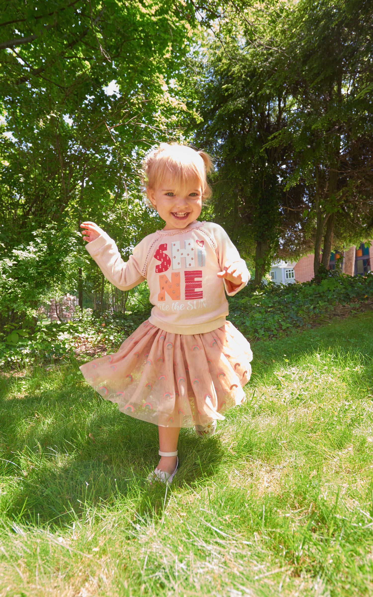 Front view of child running outside with pink sweatshirt and tulle skirt set with "shine like the sun" wording  