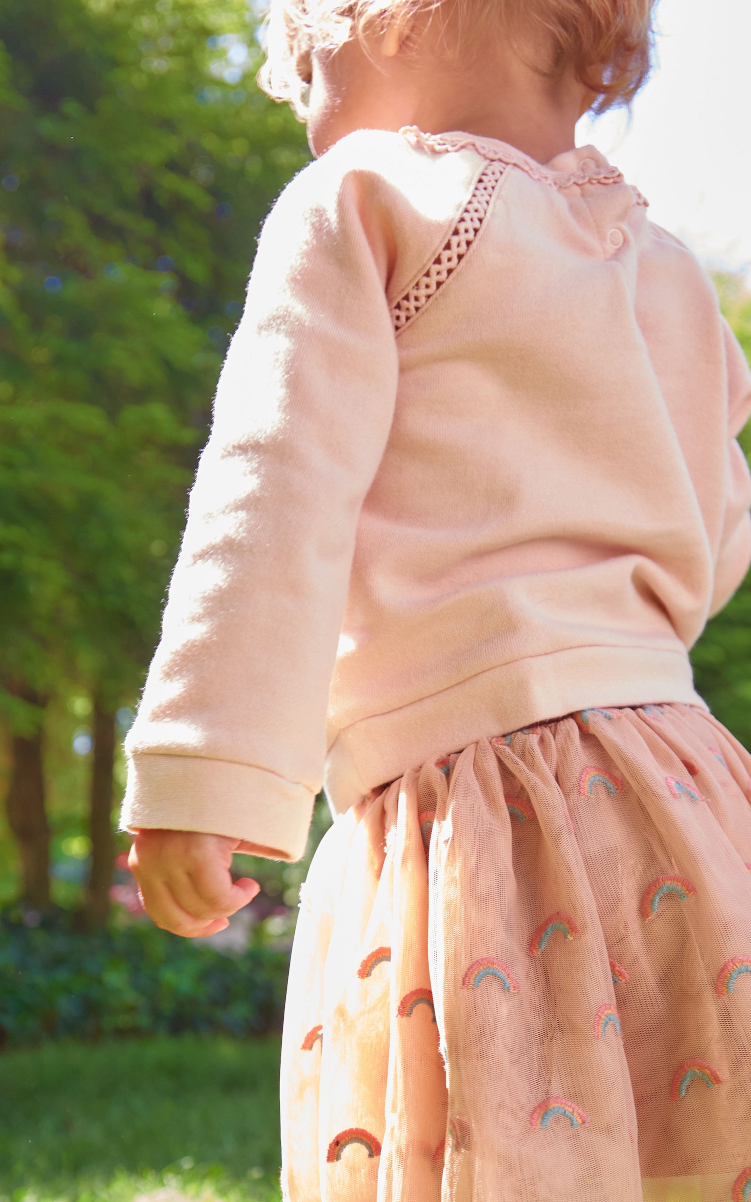 Back view of child running outside with pink sweatshirt and tulle skirt set with "shine like the sun" wording  