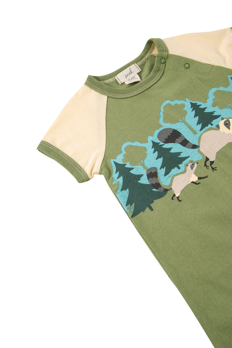 Close up of green and off-white onesie with illustrated raccoons running through a forest