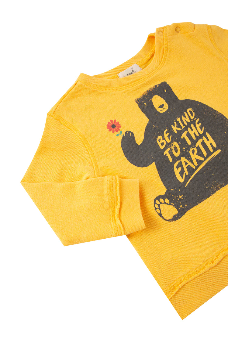 Close up of yellow sweatshirt with illustrated bear holding a flower and 'be kind to the earth' text