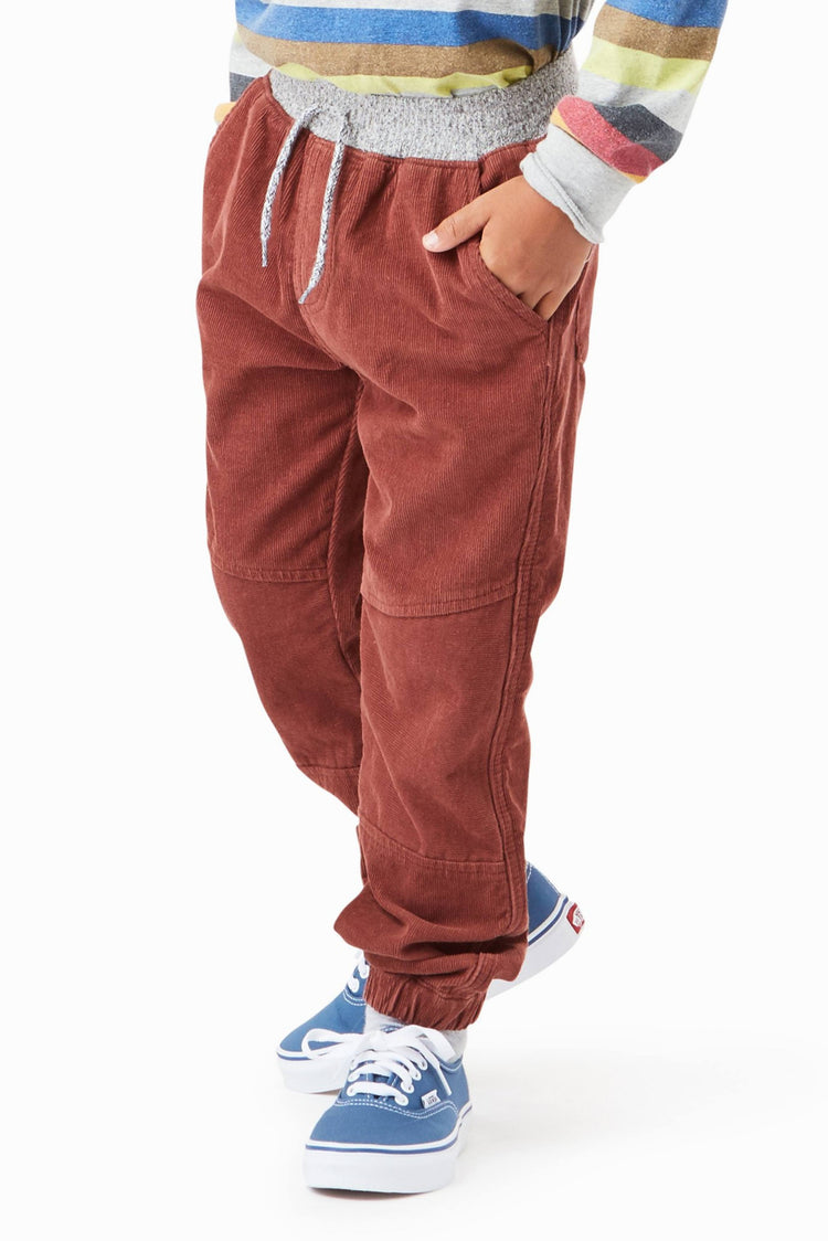 Boy wearing brown corduroy joggers with striped long sleeve shirt and blue sneakers. 
