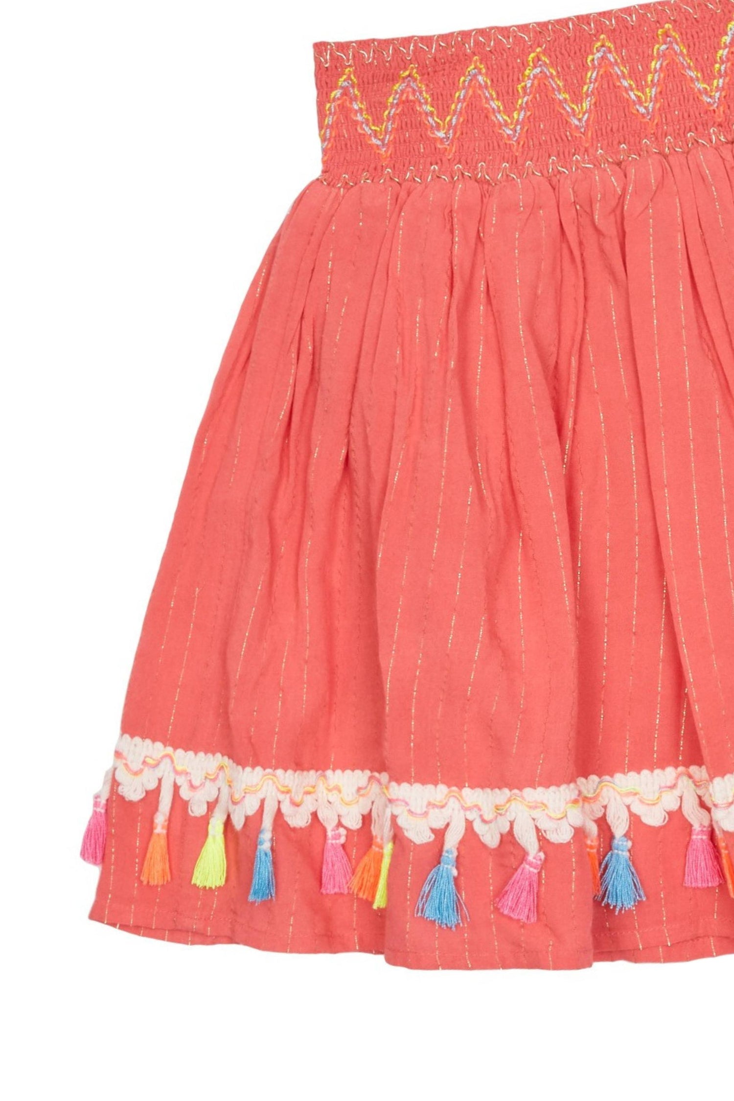 Close up of coral-colored skirt with metallic thread stripes, zig-zag stitching on waist, and embroidered fringe at hem. 